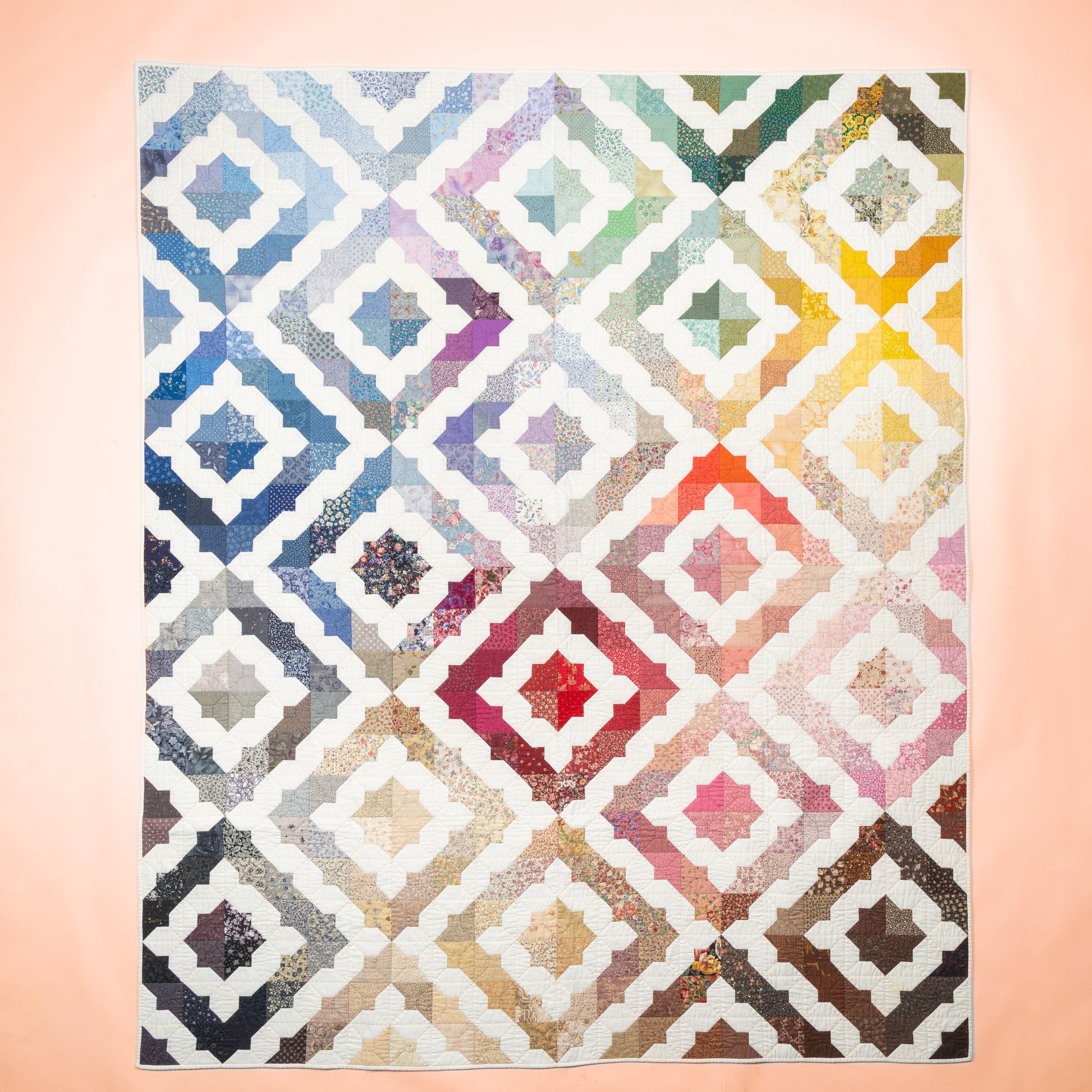A geometric quilt with repeated diamond blocks on a clean peach studio backdrop.